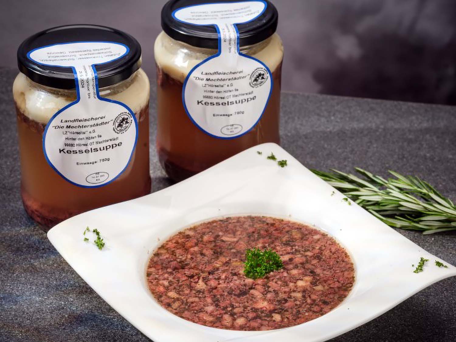 Eine Portion Kesselsuppe, angerichtet auf einem Teller mit Petersilie. Dahinter stehen zwei Gläser Kesselsuppe