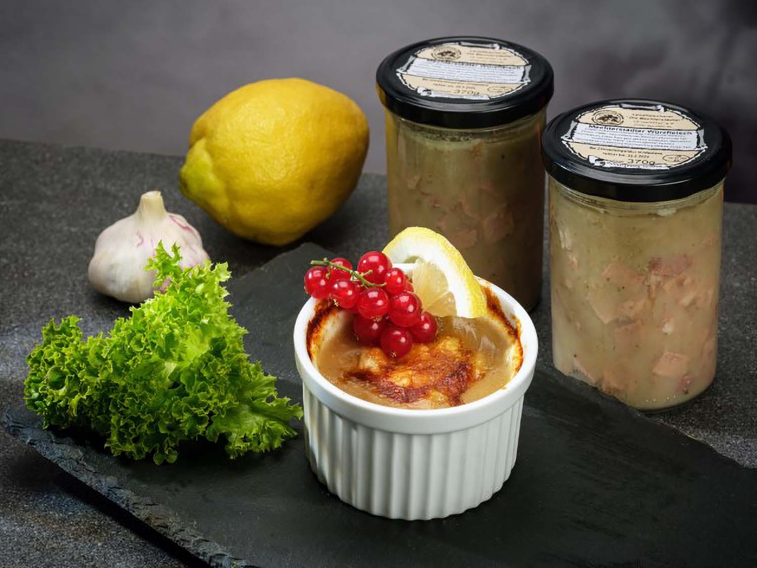 Mechterstädter Würzfleisch: Eine Portion Würzfleisch, angerichtet auf einer schwarzen Schieferplatte, mit Petersilie, Zitrone und Roten Johannisbeeren dekoriert. Im Hintergrund stehen zwei Gläser Würzfleisch