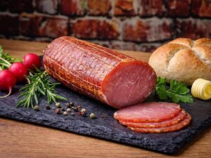 Ein aufgeschnittener Lachsschinken liegt dekorativ angerichtet auf einer schwarzen Schieferplatte