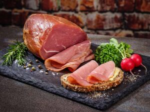 Ein aufgeschnittener Nussschinken liegt dekorativ angerichtet auf einer schwarzen Schieferplatte